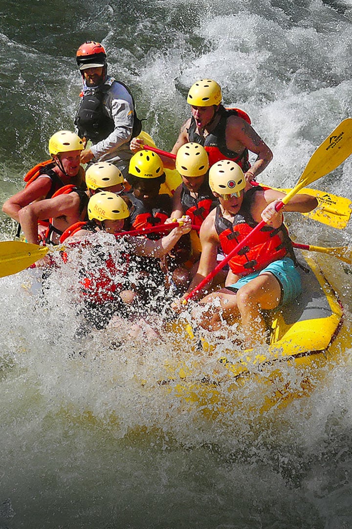 Group of eight rafters in helmets and yellow life vests powering through Royal Gorge whitewater rapids